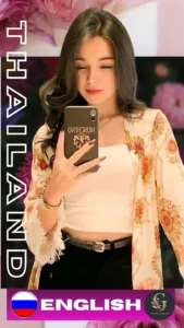 Thai woman taking a mirror selfie with a smartphone, wearing a white crop top, floral shawl, and black pants. She has long brown hair and red lips. Background includes pink and purple flowers. Text on the image reads "THAILAND" and "ENGLISH" with a Russian flag and Asian Golden Spa logo. Promotional content for Asian Golden Spa in Ras Al Khaimah.