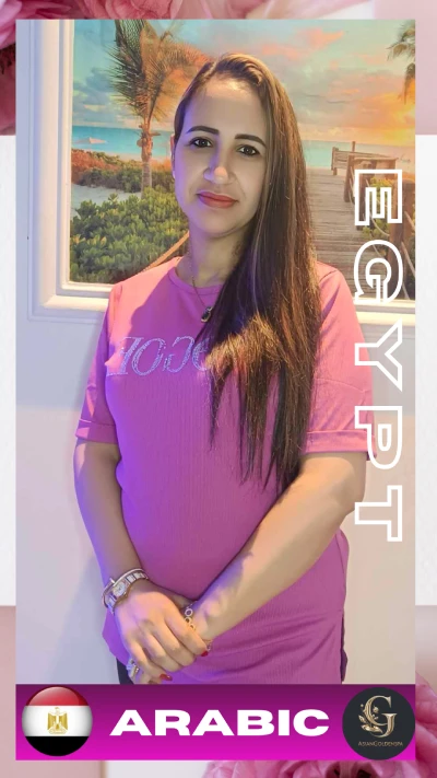 Arabic-speaking female massage therapist from Egypt wearing a pink shirt, standing in front of a beach painting with hands gently clasped, representing Egyptian staff at Asian Golden Spa in Ras Al Khaimah; offering Arabic language support for full body and oil massage in Nakheel spa center.