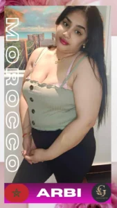 Moroccan woman posing confidently in a sleeveless green top with button details and black pants, standing indoors with a beach-themed wall art in the background. She has long black hair, red lips, and is accessorized with gold jewelry. The image includes the Moroccan flag, the word "ARBI", and the Asian Golden Spa logo. Promotional material for Asian Golden Spa in Ras Al Khaimah.