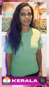 Indian woman standing and smiling at the camera, wearing a light green t-shirt and black pants, with long black hair, minimal makeup, and a butterfly necklace; background features a tropical beach scene with palm trees and sunset. Text on image includes “INDIA” vertically and “KERALA” with the Indian flag. Branding from Asian Golden Spa is visible. Location: Ras Al Khaimah, Nakheel, Prime Hotel, 1st Floor, Right Side.