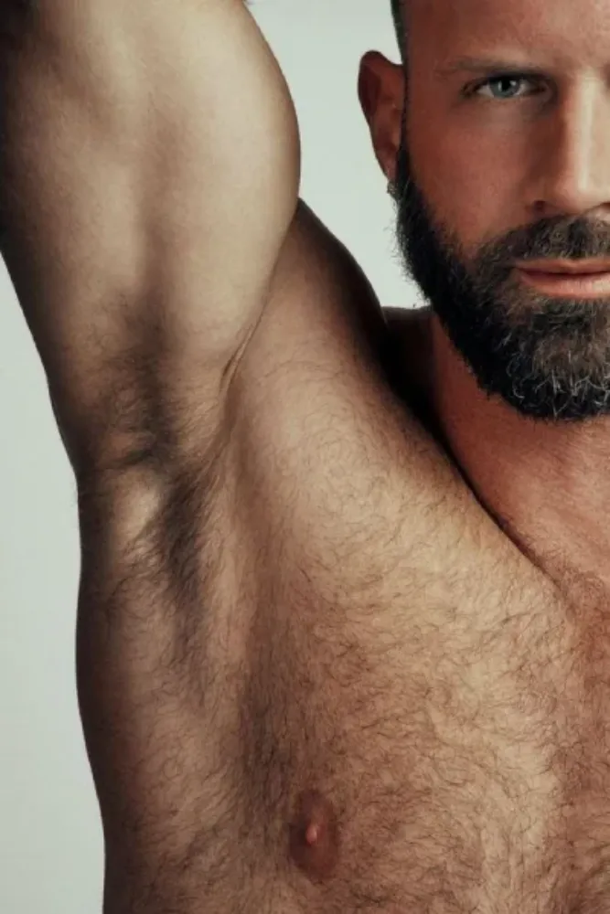 Close-up of a bearded muscular man's upper body showing his raised arm and natural underarm hair, promoting male grooming services — Asian Golden Spa, Ras Al Khaimah, Nakheel Prime Hotel, 1st Floor. Call 056 978 9770.