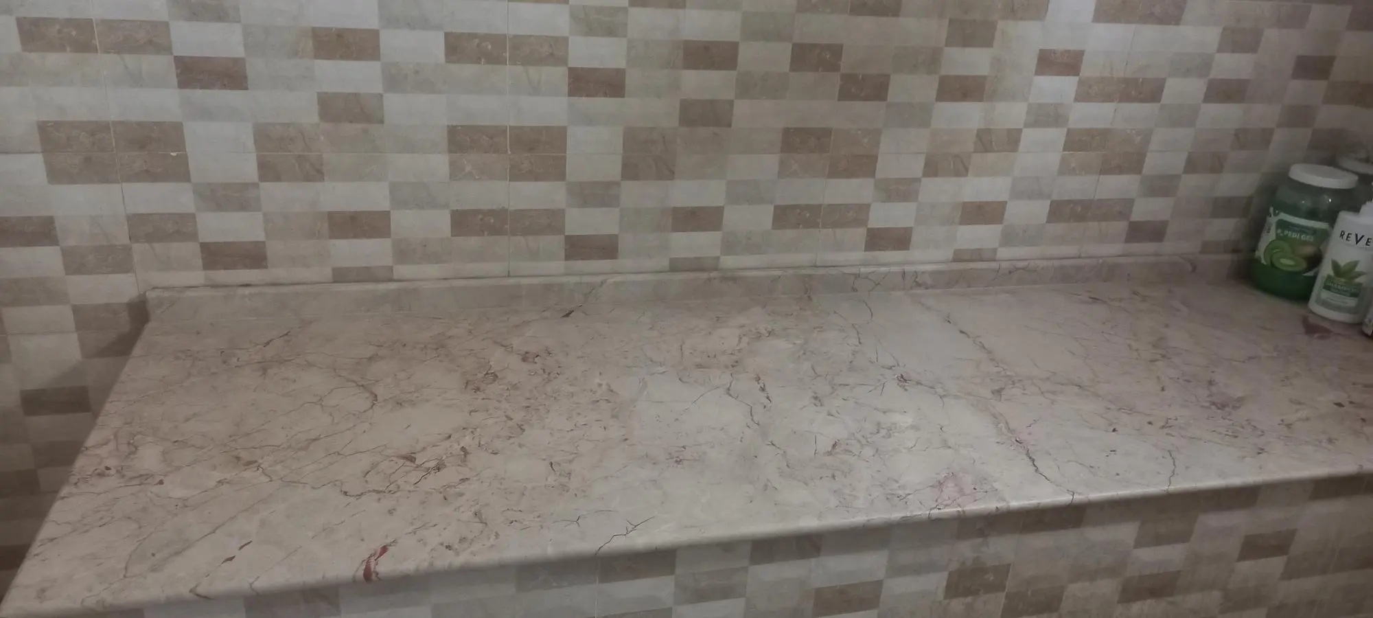 Stone massage table at Asian Golden Spa in Nakheel Prime Hotel, Ras Al Khaimah, with mosaic tiled wall, Revlon shampoo, and green aloe vera pedi gel jars placed on the corner.