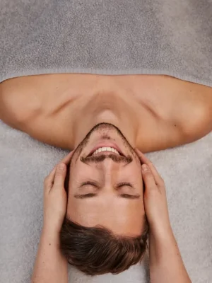 Happy man receiving a relaxing head and face massage at Asian Golden Spa, Nakheel Prime Hotel, Ras Al Khaimah – lying on spa bed with therapist holding his head