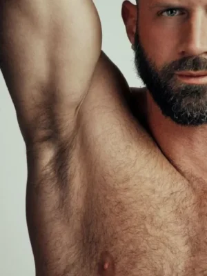 Close-up of a bearded muscular man's upper body showing his raised arm and natural underarm hair, promoting male grooming services — Asian Golden Spa, Ras Al Khaimah, Nakheel Prime Hotel, 1st Floor. Call 056 978 9770.
