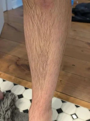 Close-up of a man's leg with natural leg hair standing on a bathroom floor, showcasing pre- or post-grooming stage—ideal for promoting leg waxing or trimming services at Asian Golden Spa, Nakheel Prime Hotel, Ras Al Khaimah. Call 056 978 9770.