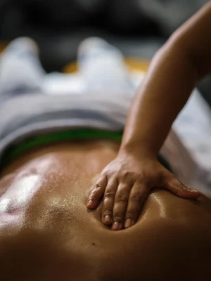A professional spa therapist performing a relaxing oil massage on a client's back at Asian Golden Spa, Ras Al Khaimah. The client is lying face down, covered with a towel from the waist down, while the therapist applies firm hand pressure to the lower back area in a serene, well-lit room.